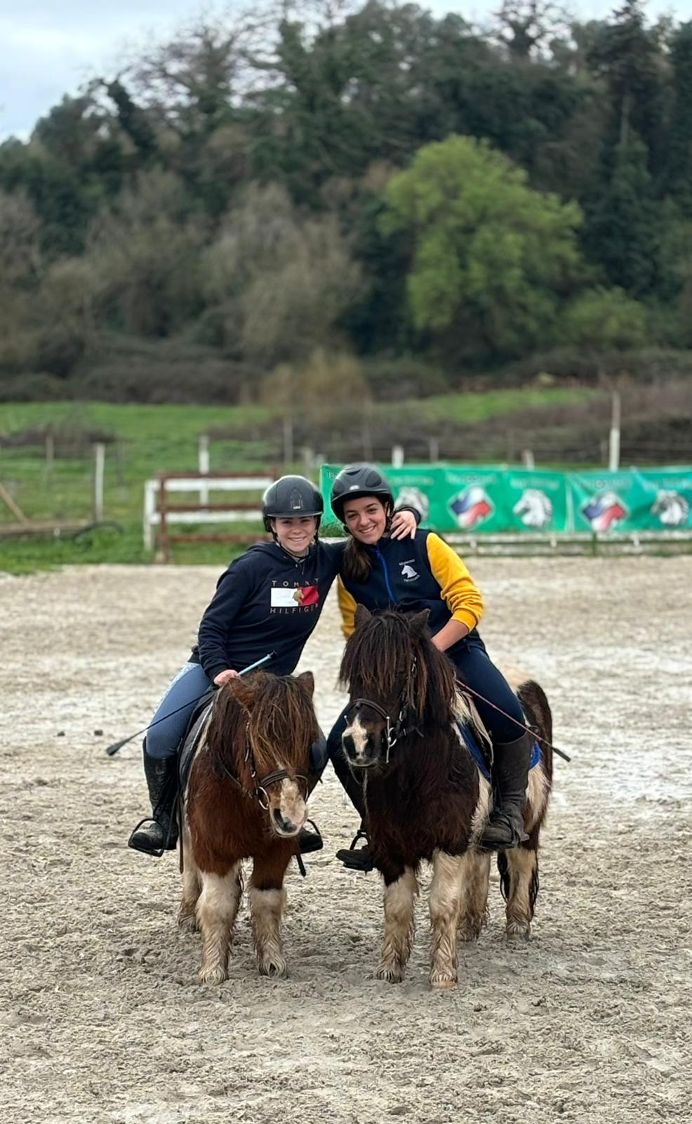 Due ragazze su pony sorridenti durante lezione al centro ippico