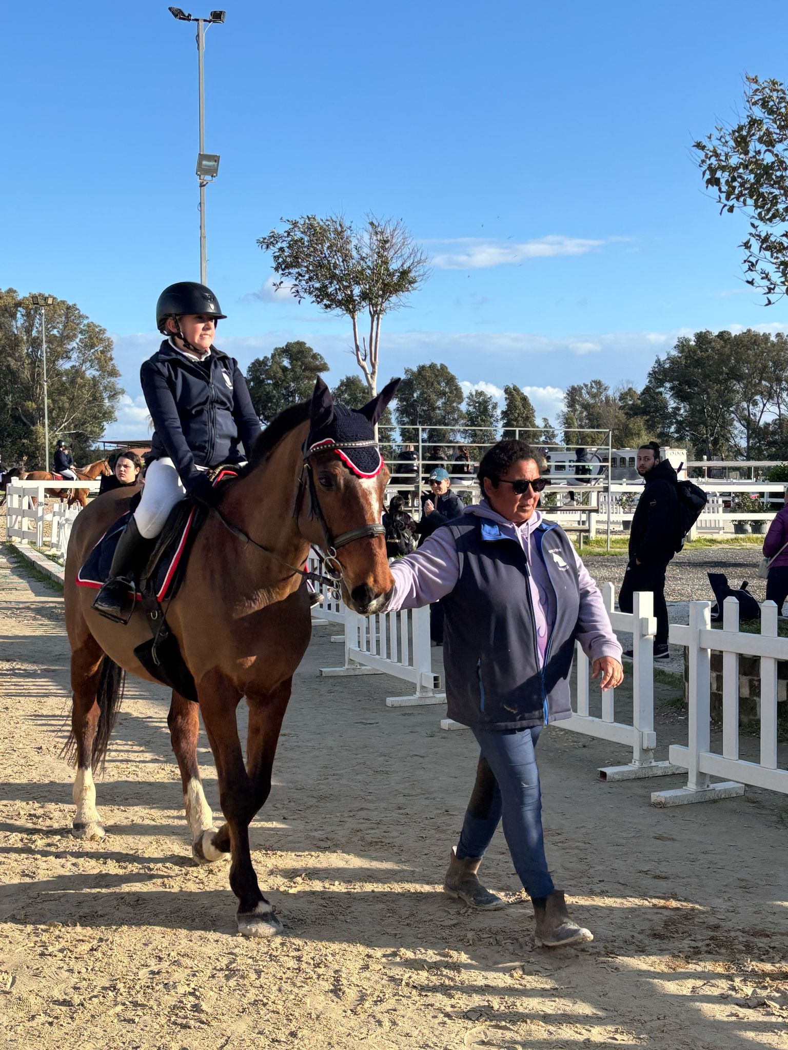 Bambina su cavallo guidata dall’istruttrice nel campo di equitazione