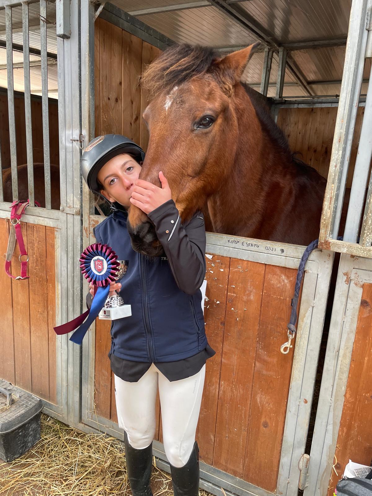 Giovane amazzone con coccarda insieme al cavallo in scuderia