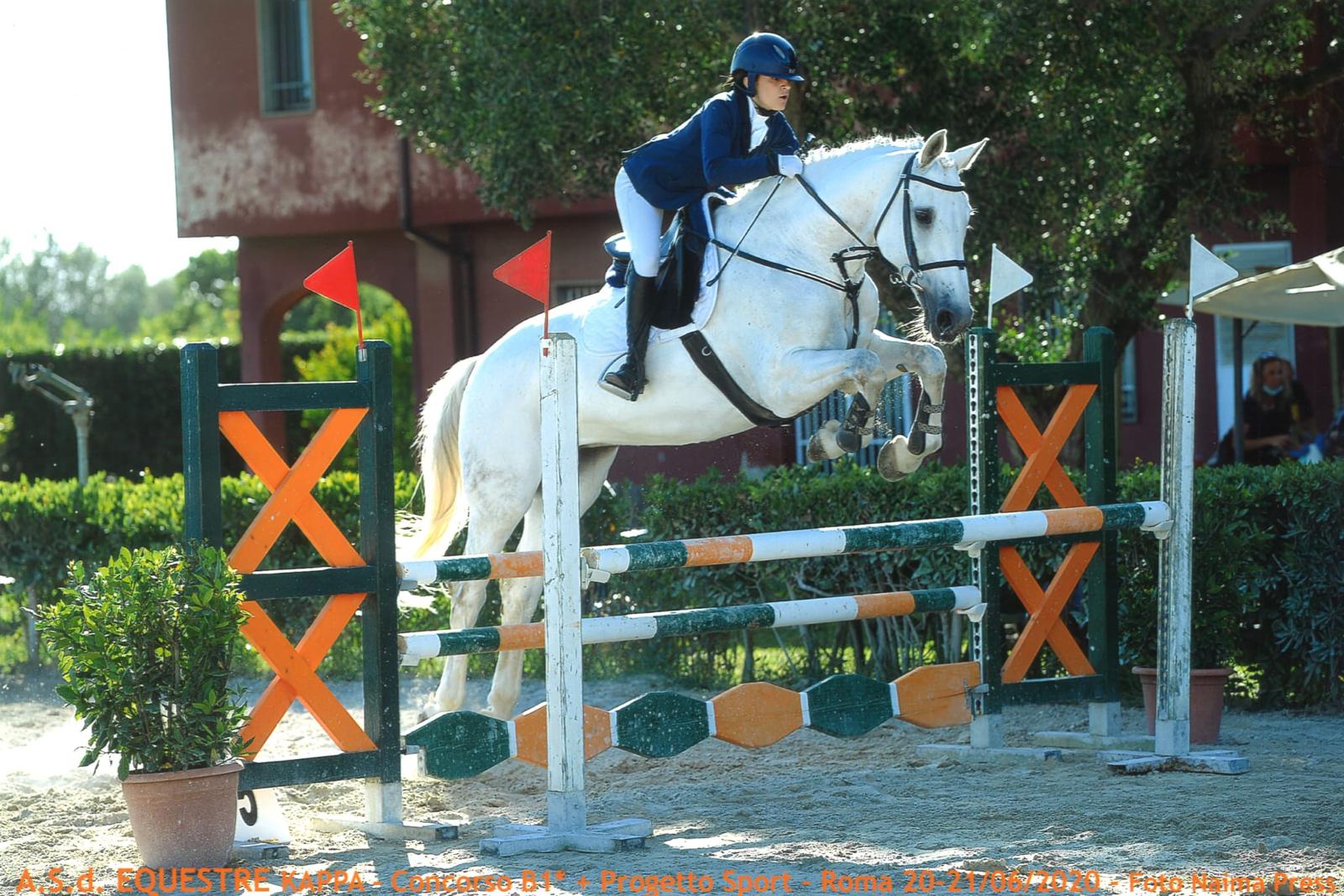 Cavallo bianco in salto su ostacolo arancione durante gara